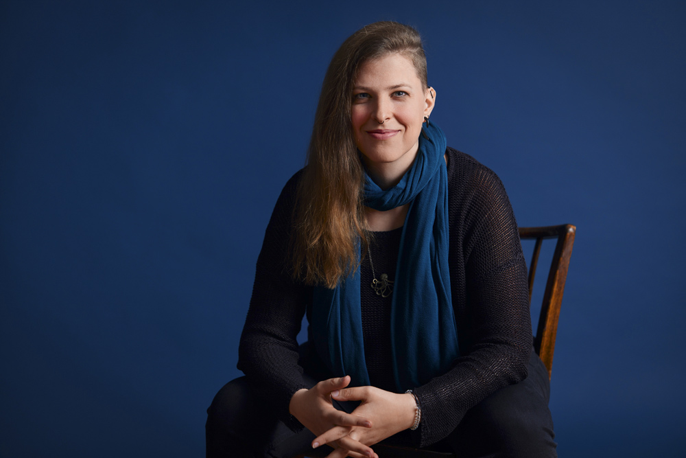 Stefanie from Corliss Design sitting on a chair in a studio smiling into the camera.
